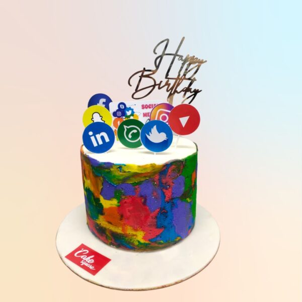 Amazing Social Media Birthday Cake 1 Kg. A square cake decorated with edible social media icons including Facebook, Instagram, Twitter, and WhatsApp logos. The cake is covered in smooth white fondant with vibrant blue and purple accents. "Happy Birthday" is written in elegant script across the top.