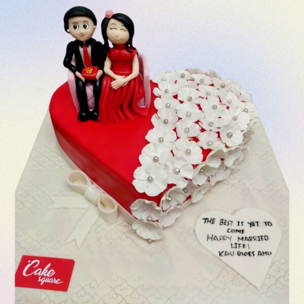 A red heart shape cake, one side of the heart has a fondant couple and the other side is filled with petunia flowers and a heart felt message in our Anniversary heart shape Cake 2 Kg made by Cake Square Chennai.