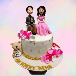 A white cake jewelled with golden sprinkle and couple sitting on a sofa with a little teddy by the side is Best Couple 1 Kg Anniversary Cake made by Cake Square team.