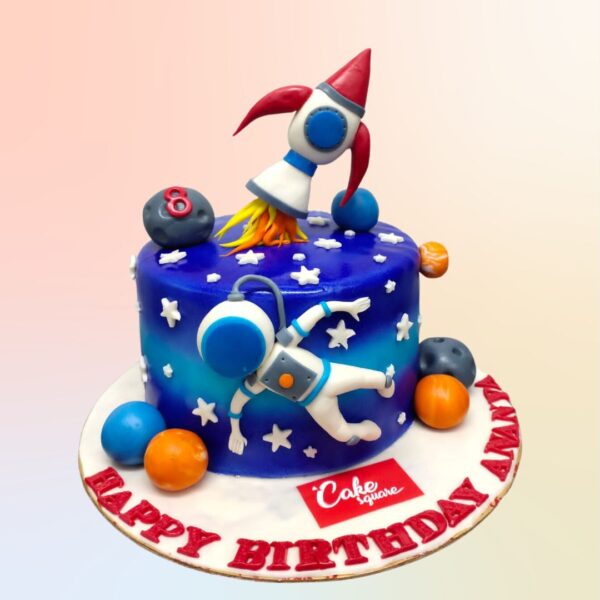 Best Rocket Theme Astronaut Kids Birthday Cake 2 Kg. Space-themed birthday cake shaped like a rocket, decorated with stars, planets, and an astronaut figure. Blue and silver icing with "Happy Birthday" message. 2 kg size perfect for parties.