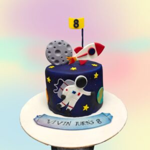 Best Special Space Theme Kids Birthday Cake 2 Kg. A round two-tier cake decorated with a cosmic space theme. The bottom tier features a starry night sky, while the top tier resembles a planet with swirling colors. Fondant astronauts, rockets, and planets orbit the cake. A fondant banner reads "Happy Birthday" in a futuristic font.