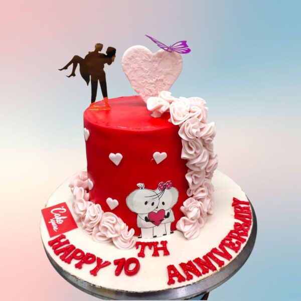 A red cake with a man carrying woman topper and a cute puppy love images on the front with a big 3d heart and a butterfly is our Crossing Threshold 1 Kg Anniversary Cake.