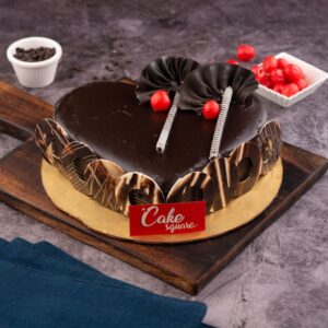 A heart-shaped 1 Kg Exotic Chocolate Birthday Cake with dark ganache coating, decorated with chocolate frills.