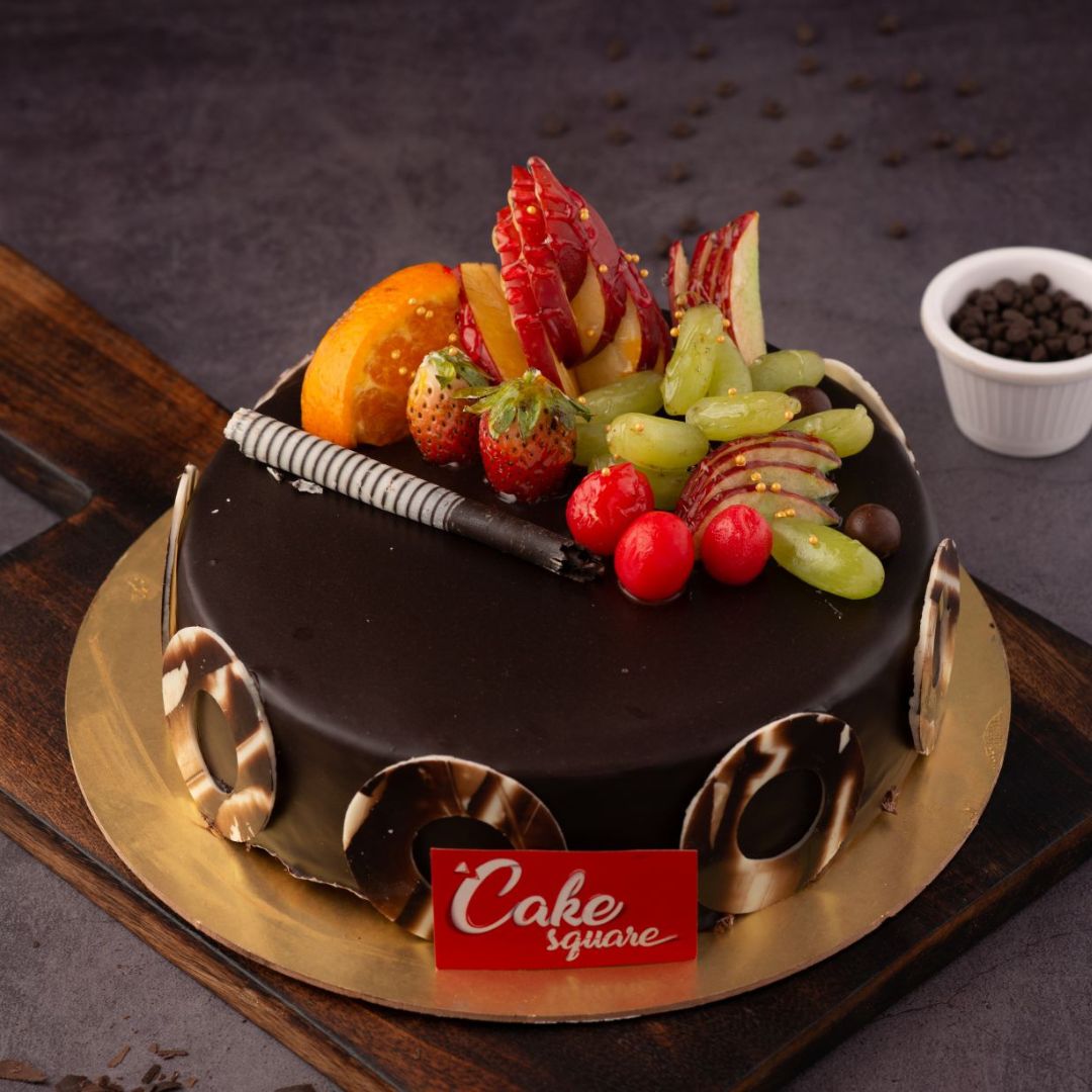 A round 1 kg Fruit Chocolate Birthday Cake with ganache coating, topped with an array of glazed fresh fruits.