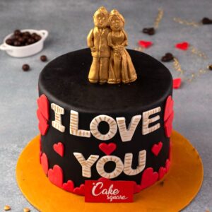 A couple topper in edible gold on a chocolate cake with red hearts and wordings I love you in Golden Couple 1 Kg Anniversary Cake by Cake Square Team.