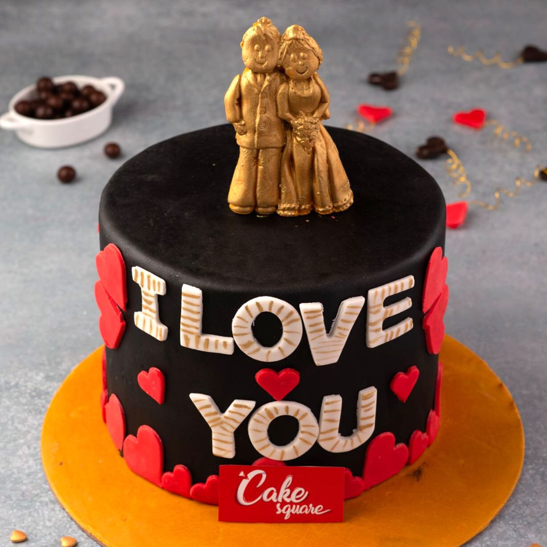 A couple topper in edible gold on a chocolate cake with red hearts and wordings I love you in Golden Couple 1 Kg Anniversary Cake by Cake Square Team.