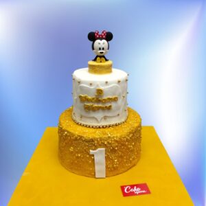 Luxurious Golden Minnie First Birthday Cake 4 Kg with shimmering gold fondant, signature polka dot bow, and "1st" tiara topper, surrounded by edible Mickey-shaped macarons.