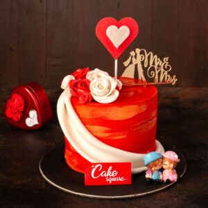 Bunch of roses and a double heart with a red cake wrapped adorn this Love Beauty 1 Kg Anniversary Cake by Cake Square Chennai.