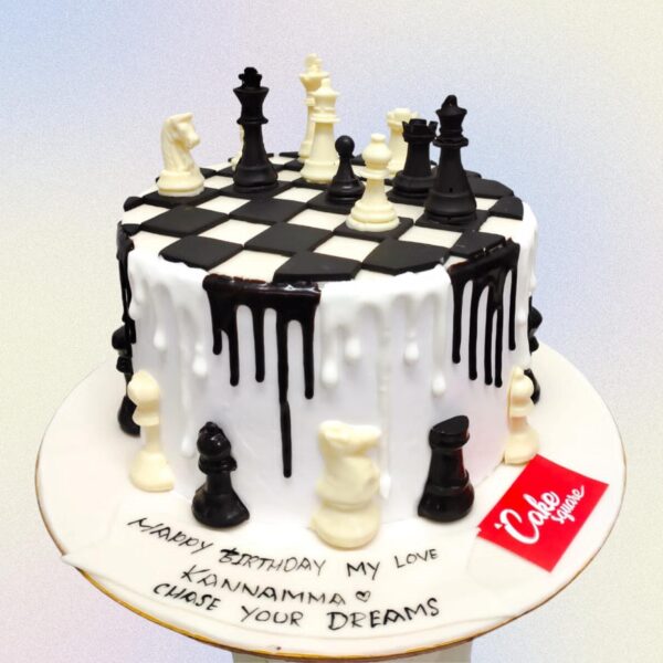 Perfect Chess Birthday Cake 1 Kg designed as a 3D chessboard with raised edges. Black and white fondant squares cover the top, with a selection of detailed fondant chess pieces. "Happy Birthday" is written on the side in an elegant script.