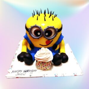 Eye-catching Stunning Minion Kids Birthday Cake 3 Kg with vibrant yellow fondant, 3D goggle eyes, blue overalls, and mischievous grin, surrounded by banana-shaped cake pops.