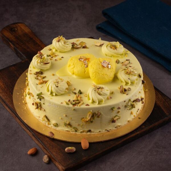 A round 1 Kg cake with smooth, pale yellow frosting, adorned with crushed nuts and real rasamalais.