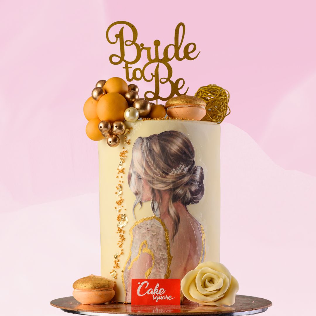 A cream colour cake with a fancy womans art on the front with couple of chocolate made faux balls and macaroons with a cake topper that says bride to be is our Amazing Bride to be Cakes 2 Kg. Made by Cake Square Team.