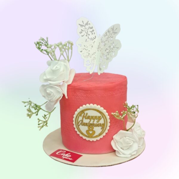 A red cake with white roses and a couple butterfly on top in chocolate flavour in this Best Peach 1 Kg Anniversary Cake by Cake Square Team