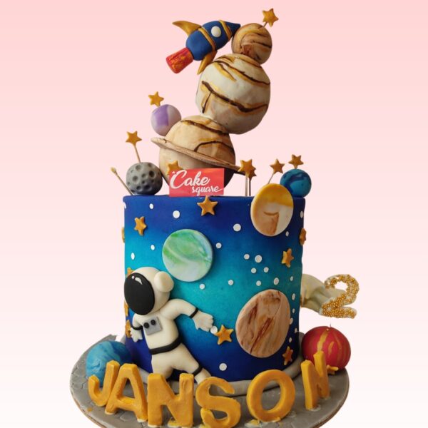 Colorful Amazing Rocket Themed Boys Birthday Cake 2 kg. Two-tiered blue and white fondant cake with red accents, decorated with edible stars, planets, and a large rocket ship topper. Perfect for space enthusiasts.