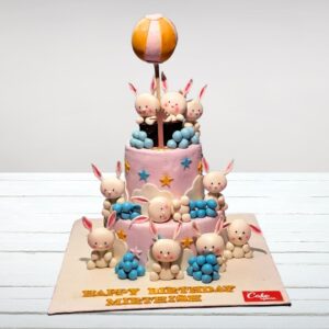 "A 5 kg first birthday cake shaped like a cute bunny, with pink and white fondant, floppy ears, and a '1' shaped carrot topper."