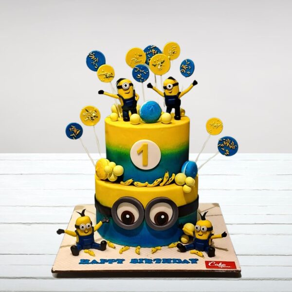 "A 5 kg first birthday cake decorated to resemble a Minion character, featuring blue and yellow fondant, googly eyes, and a '1' shaped topper."