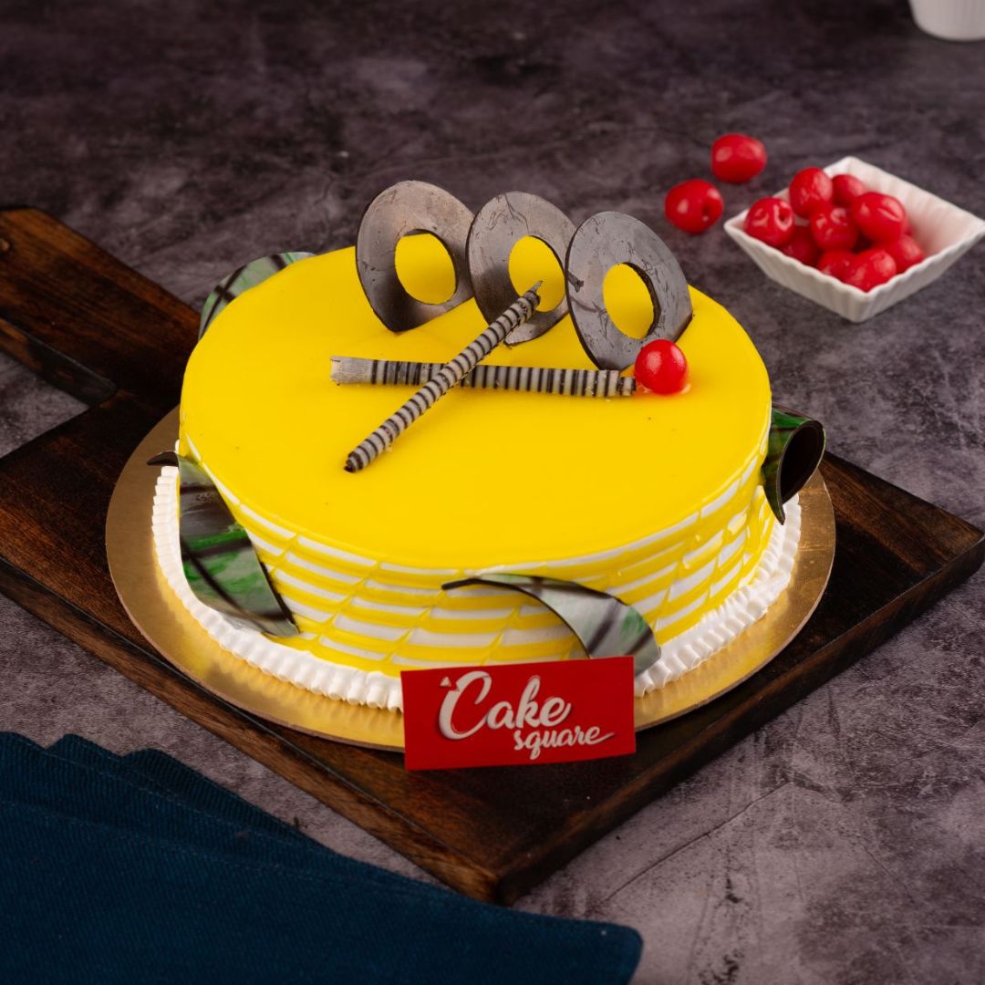 A yellow 1 Kg cake with couple of cherries and chocolate ganche filled with juicy pineapple in this Delicious Pineapple 1 kg Birthday Cake made by Cake Square