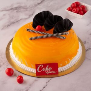 An orange real mango cake in a vanilla sponge decorated with chocolate sticks and cherry is our Elegant Mango Half Kg Birthday Cake by Cake Square Team