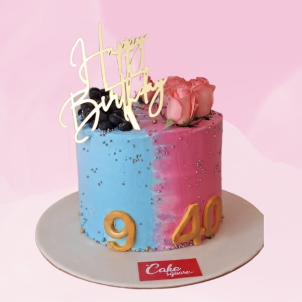 A 1 kg cake split into two halves, each representing a twin. The left side is blue for the boy, decorated with tiny fondant cars and footballs. The right side is pink for the girl, adorned with small fondant flowers and butterflies. In the center, where the halves meet, there's a fondant number "1/2" to signify six months. The cake is round and covered in smooth cream. On top, two fondant baby figures - a boy in blue and a girl in pink - sit side by side. The cake's border is decorated with alternating blue and pink rosettes.