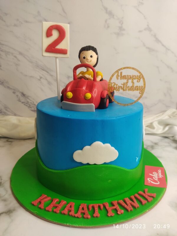 Boy in car Customised Birthday Cake 1kg, featuring a fondant boy figurine driving a colorful car-shaped cake.