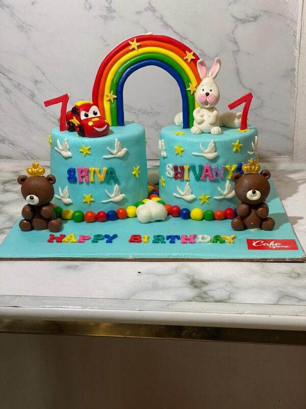 Two Cakes connected with a rainbow and customised to each of thier favourite toys and names written in multi colour fondant letters. Made by Cake Square Chennai Team