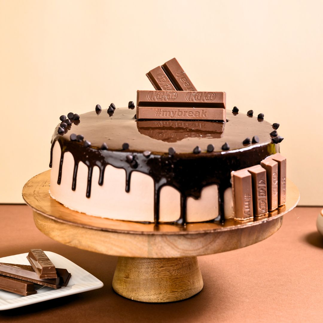 "Decadent Kitkat Birthday Cake 1 Kg featuring chocolate layers surrounded by crispy KitKat fingers, topped with chocolate ganache, Gems, and chocolate drips for the ultimate celebration cake"